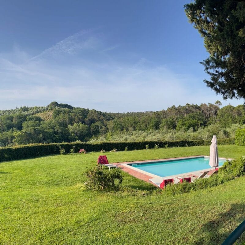 Outdoor swimming pool on a Tuscan villa property surrounded by a green lawn and forested hills